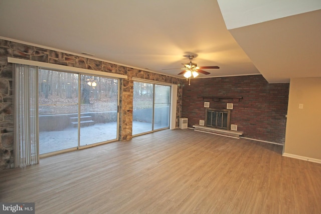 unfurnished living room featuring ceiling fan, brick wall, hardwood / wood-style floors, and a brick fireplace