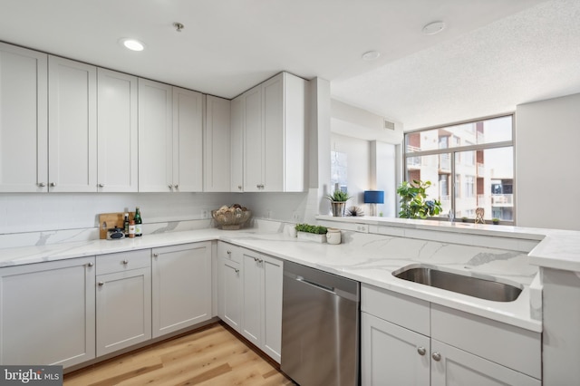 kitchen featuring sink, light wood-type flooring, stainless steel dishwasher, and light stone counters