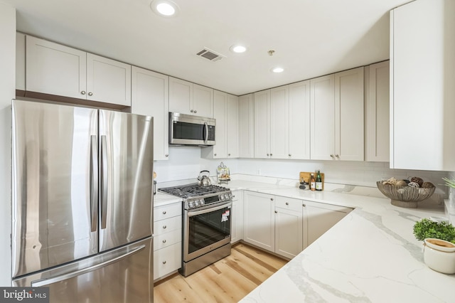 kitchen with light stone counters, white cabinetry, light hardwood / wood-style floors, and appliances with stainless steel finishes