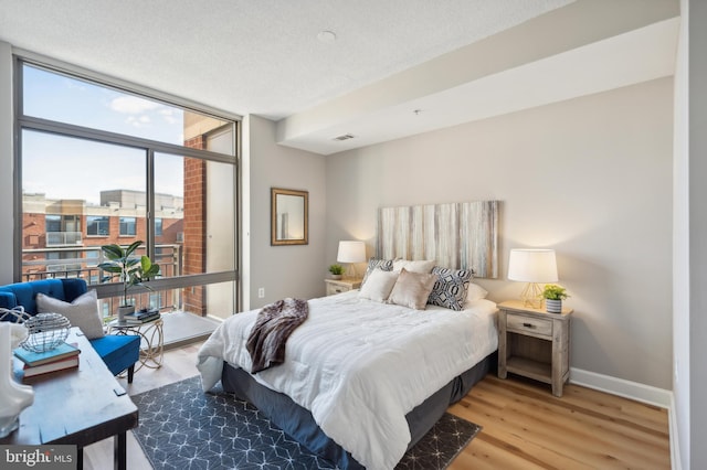 bedroom featuring light hardwood / wood-style floors, expansive windows, and a textured ceiling