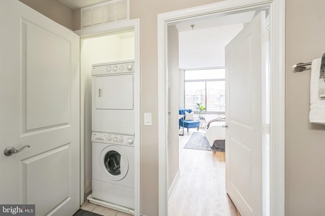 clothes washing area with stacked washing maching and dryer and light hardwood / wood-style floors