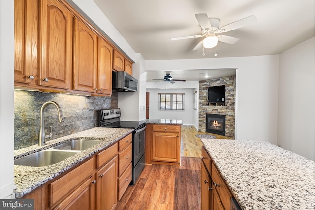 kitchen featuring a sink, light stone counters, appliances with stainless steel finishes, brown cabinetry, and dark wood-style flooring