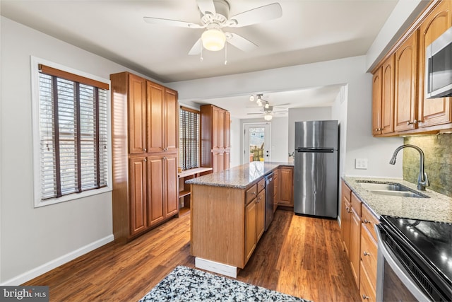 kitchen featuring light stone counters, dark wood-style flooring, appliances with stainless steel finishes, and a sink