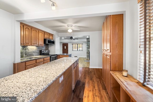 kitchen with brown cabinetry, dark wood finished floors, stainless steel appliances, and a sink