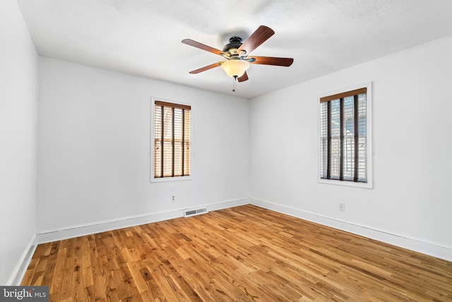 empty room with a ceiling fan, wood finished floors, a healthy amount of sunlight, and visible vents