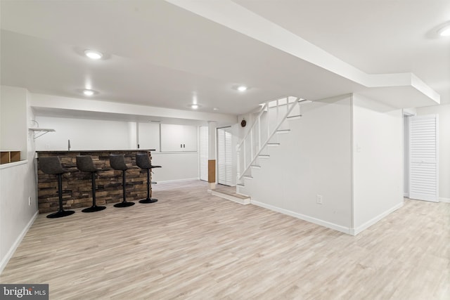 finished basement with baseboards, stairs, indoor wet bar, recessed lighting, and wood finished floors