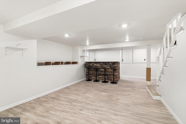 finished basement featuring a bar, recessed lighting, baseboards, and light wood-type flooring