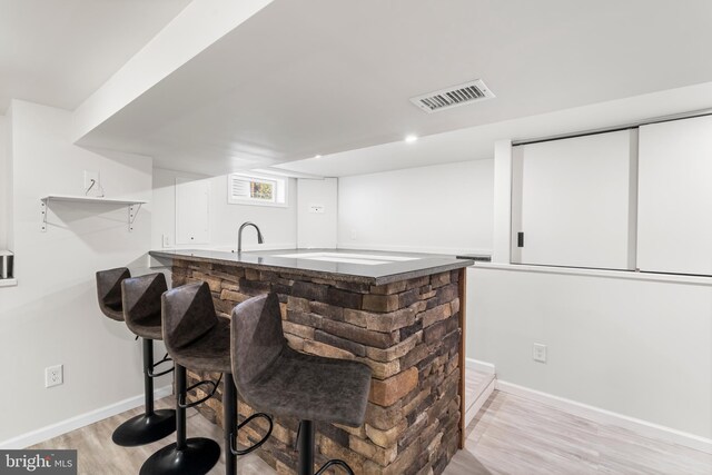 bar with visible vents, baseboards, indoor wet bar, and light wood finished floors