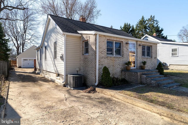 view of front of property featuring an outbuilding, central AC, a chimney, a detached garage, and brick siding