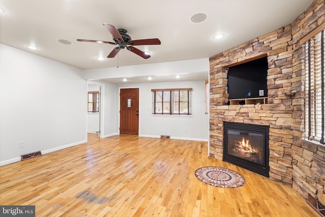 unfurnished living room featuring wood finished floors, visible vents, baseboards, ceiling fan, and a stone fireplace