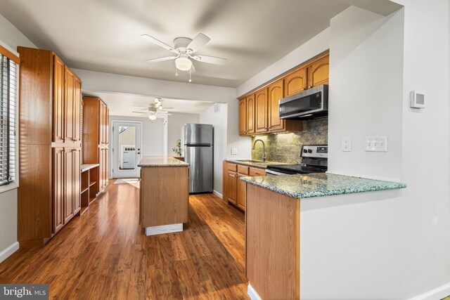 kitchen featuring backsplash, a kitchen island, dark wood finished floors, stainless steel appliances, and a sink