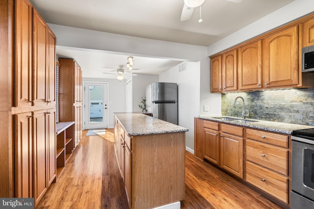 kitchen with a sink, backsplash, a center island, appliances with stainless steel finishes, and light stone countertops