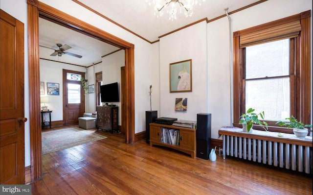 entrance foyer featuring wood-type flooring, radiator, ceiling fan with notable chandelier, and ornamental molding