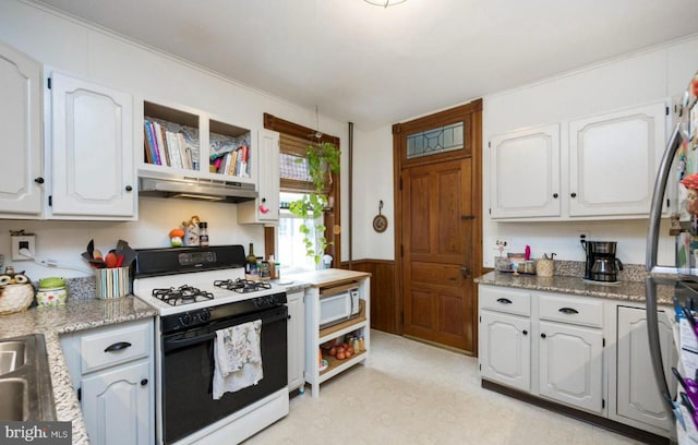 kitchen featuring white cabinetry, light stone countertops, gas range oven, and wood walls