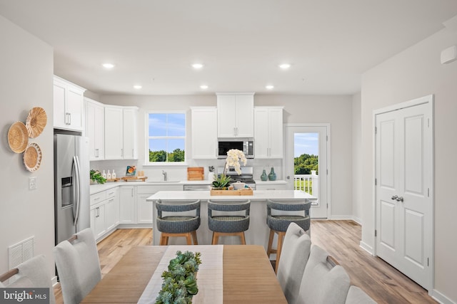 kitchen with a kitchen bar, stainless steel appliances, light hardwood / wood-style floors, white cabinets, and a kitchen island