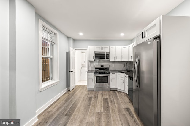 kitchen featuring sink, appliances with stainless steel finishes, light hardwood / wood-style floors, white cabinets, and decorative backsplash