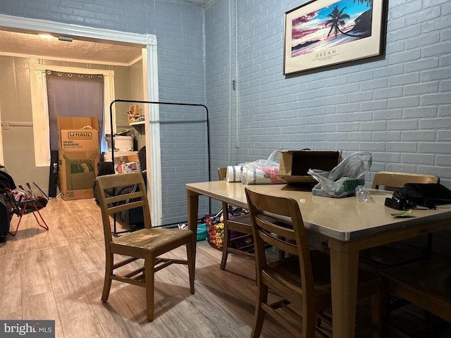 dining space with crown molding, light hardwood / wood-style flooring, and brick wall