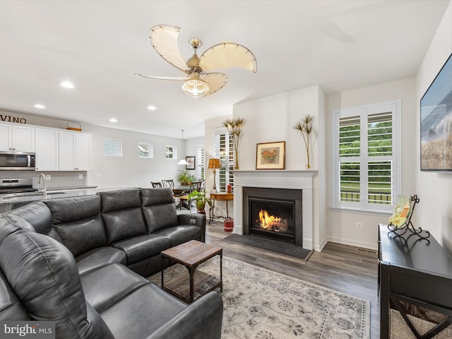 living area with a warm lit fireplace, recessed lighting, wood finished floors, and baseboards