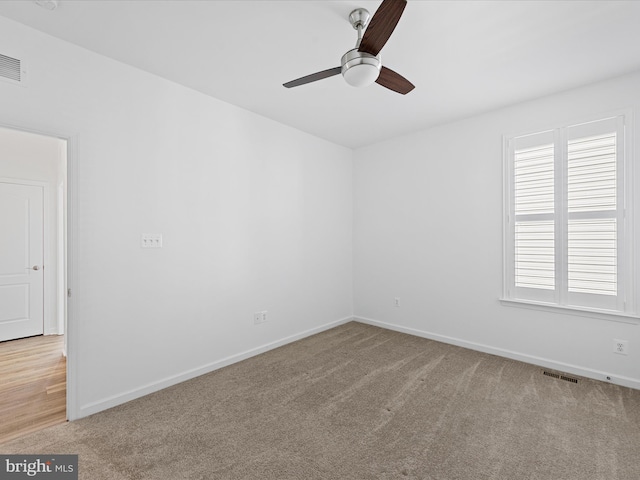 spare room with a ceiling fan, light colored carpet, visible vents, and baseboards