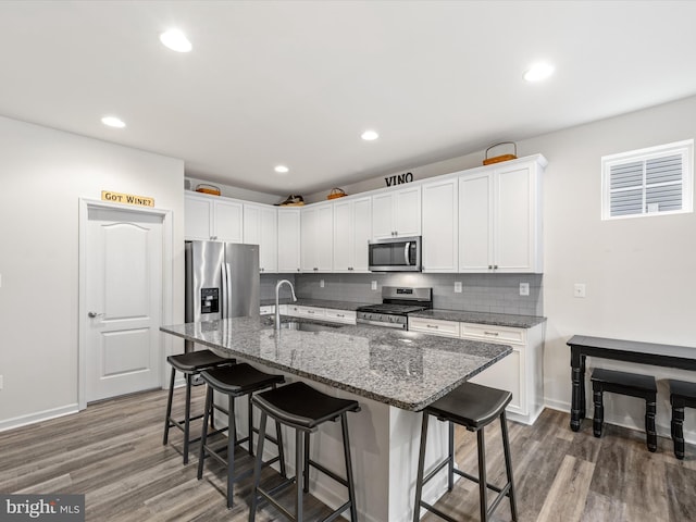 kitchen featuring stainless steel appliances, wood finished floors, a sink, backsplash, and a kitchen bar