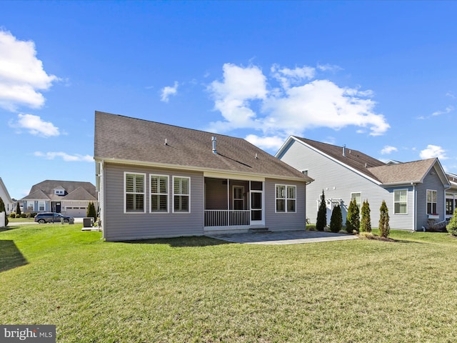 rear view of house with a shingled roof, a sunroom, a patio area, and a yard