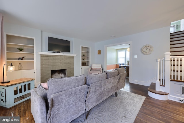 living room with dark wood-type flooring, a brick fireplace, and built in features