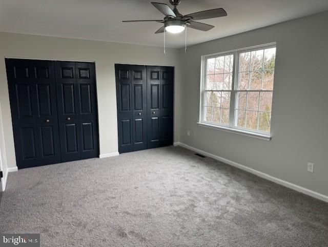 unfurnished bedroom with two closets, ceiling fan, and carpet flooring