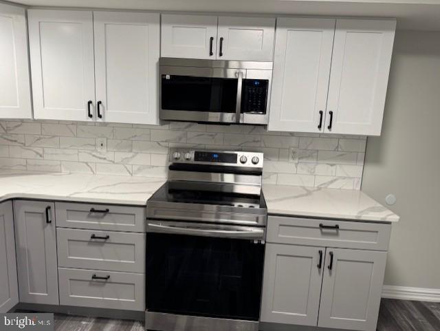 kitchen with tasteful backsplash, stainless steel appliances, light stone countertops, and white cabinets