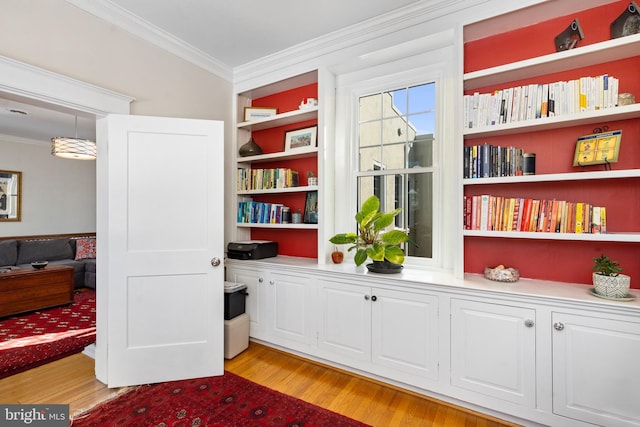 sitting room featuring light wood-style flooring, built in features, and crown molding