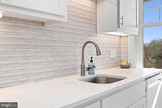 kitchen featuring white cabinets, backsplash, light countertops, and a sink