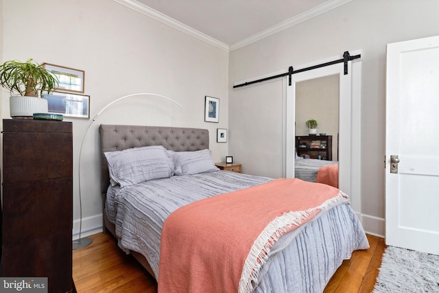 bedroom featuring light wood-type flooring, a barn door, baseboards, and crown molding