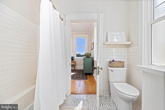 bathroom featuring a wainscoted wall, tile walls, toilet, shower / bath combo with shower curtain, and tile patterned floors