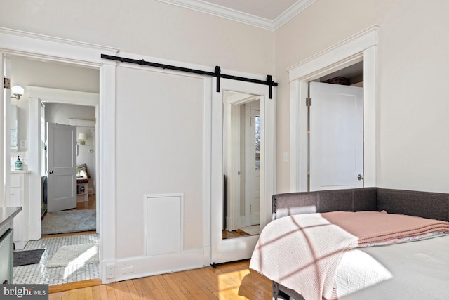 bedroom with crown molding, light wood-style flooring, and a barn door