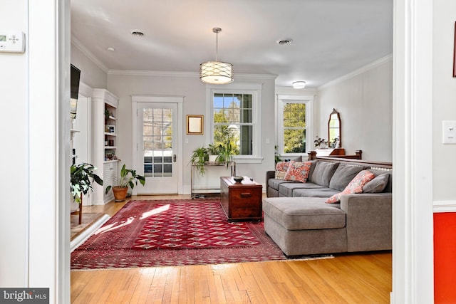 living area featuring a healthy amount of sunlight, crown molding, visible vents, and wood finished floors