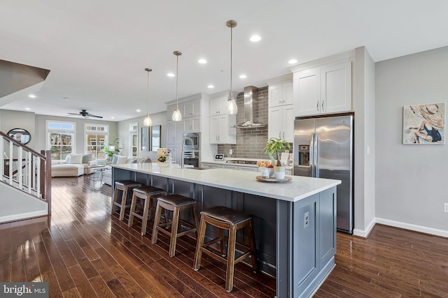 kitchen featuring a spacious island, decorative light fixtures, wall chimney range hood, stainless steel appliances, and white cabinets