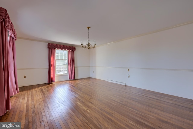 spare room with hardwood / wood-style flooring, ornamental molding, baseboard heating, and an inviting chandelier