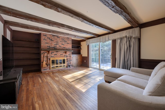 living room with built in shelves, a fireplace, beamed ceiling, and wood-type flooring