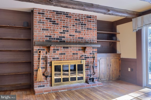 unfurnished living room featuring beamed ceiling, wooden walls, a fireplace, and light hardwood / wood-style floors