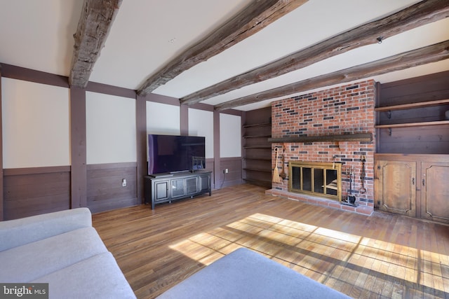 living room featuring beam ceiling, a fireplace, wood walls, and light wood-type flooring