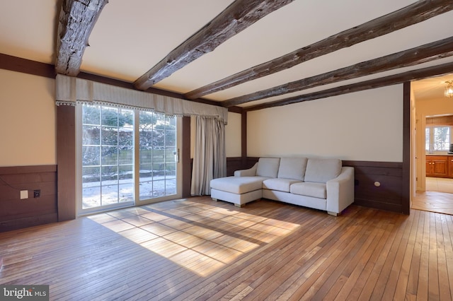 unfurnished living room with beamed ceiling and light wood-type flooring