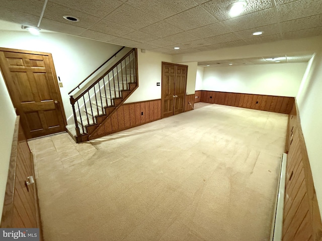 basement with light carpet, a paneled ceiling, and wood walls