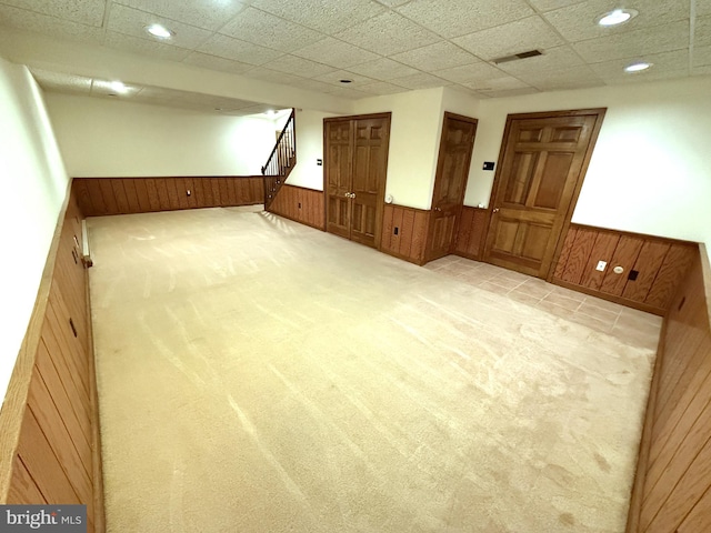 carpeted empty room featuring a paneled ceiling and wood walls