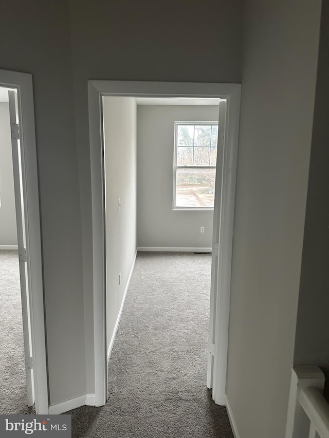 corridor with baseboards and dark carpet