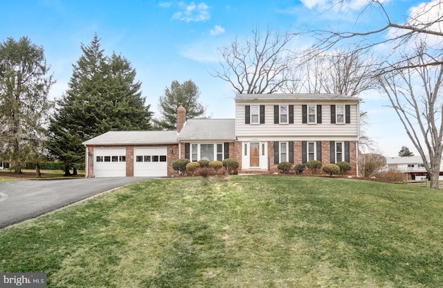 colonial home featuring brick siding, a chimney, an attached garage, driveway, and a front lawn