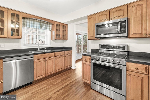 kitchen featuring stainless steel appliances, dark countertops, light wood-style flooring, brown cabinetry, and a sink