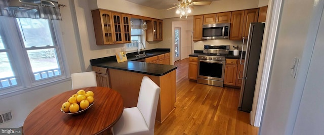 kitchen with light wood finished floors, dark countertops, brown cabinets, a peninsula, and stainless steel appliances