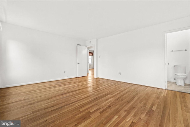 unfurnished bedroom with light wood-style flooring, baseboards, and ensuite bathroom