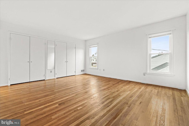 unfurnished bedroom with light wood-type flooring, visible vents, baseboards, and multiple closets