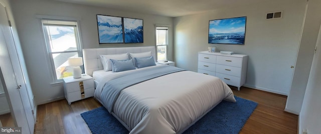 bedroom with multiple windows, wood finished floors, visible vents, and baseboards