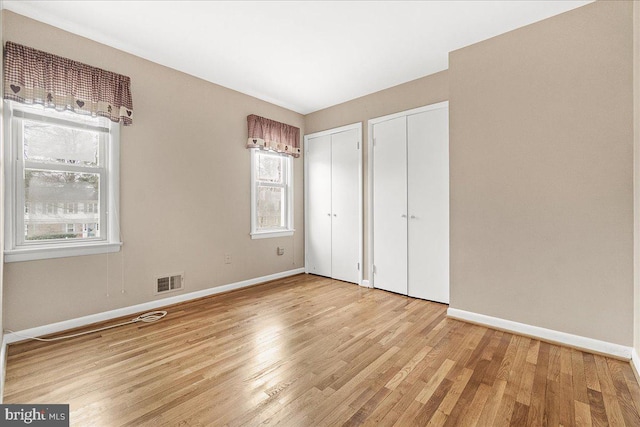 unfurnished bedroom featuring multiple closets, light wood-type flooring, visible vents, and baseboards